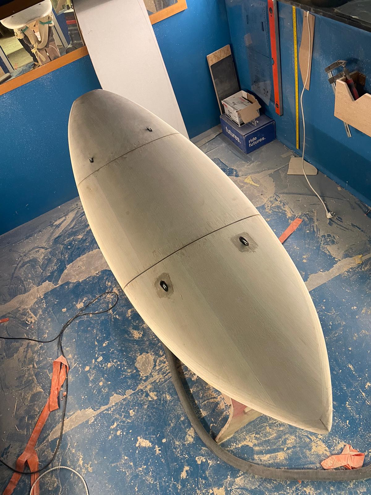 Fiberglass and foam prototype of the ATACH surfboard in the workshop, showing the three-part assembly.